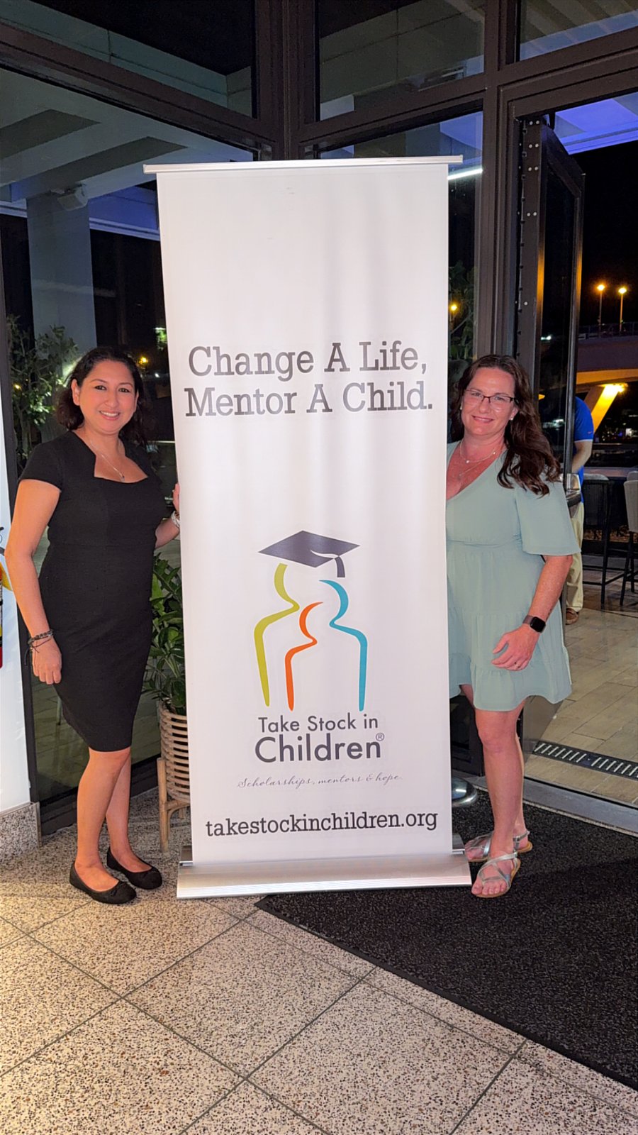 Two people beside a Change A Life, Mentor A Child banner at a Take Stock event